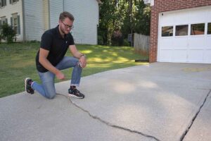 Photo of a man inspecting a cracked, uneven concrete residential driveway in need of concrete repair and leveling.